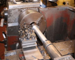 Meanwhile, in the machine shop we see the seventh of twelve pins for the spring hanger brackets being turned. This is a flash shot so the lathe chuck appears stationary despite spinning at several hundred RPM.