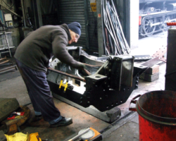 The pony truck continues its isolated existence at the south end of the works but has not been forgotten. It has been turned over to allow access to the underneath parts, to which a Fund member is applying grey primer paint.