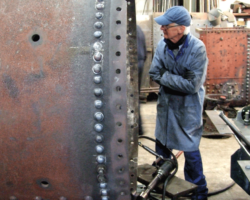 More riveting, securing the front tubeplate to the barrel. One of the SMF painters peers speculatively at the tubeplate; does he intend to attack this with his paintbrush too?